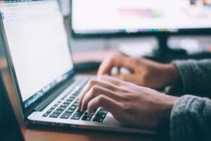 Pessoa mexendo em um notebook com o foco em suas mãos