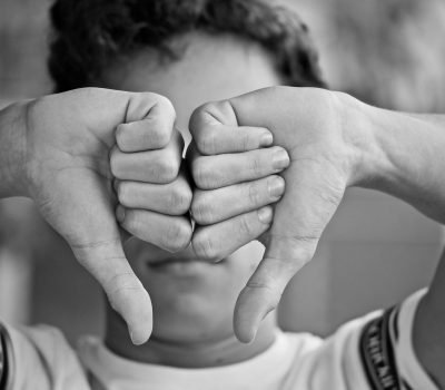 Foto em preto e branco de garoto com polegares para baixo na frente de seu rosto